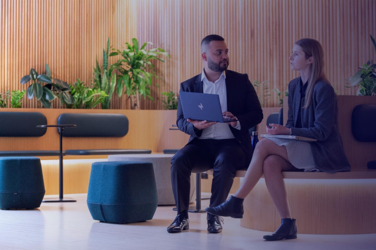 Two cyber security consultants in an open office talking while holding laptops